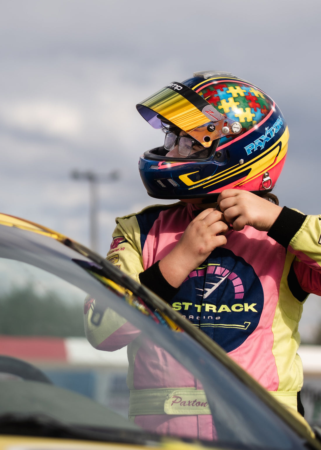 Fast Track Racing driver Paxton fastening his helmet beside the race car